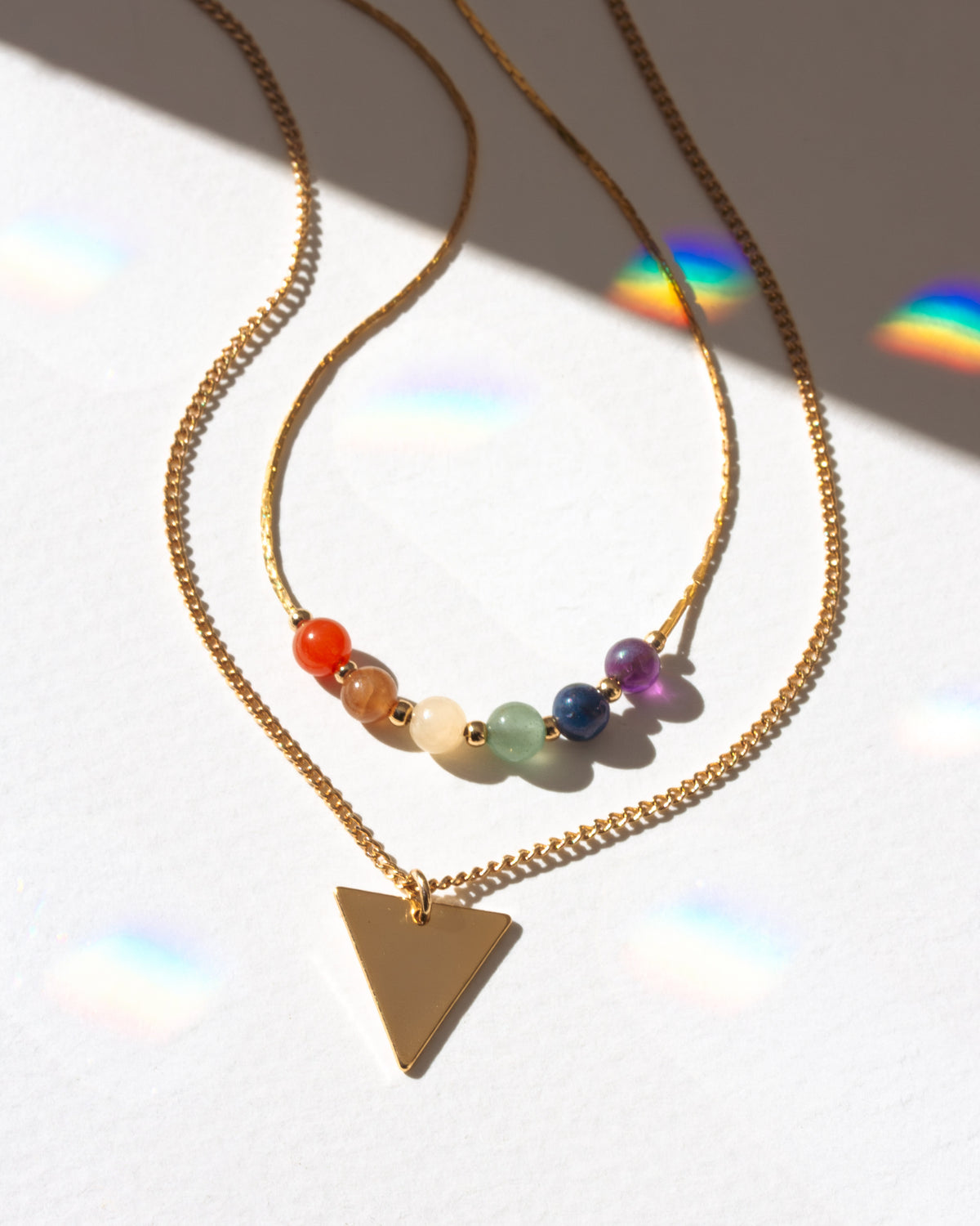 Gold necklace with colorful beads and a triangle pendant on a white background