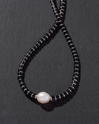 Necklace with black beads and a pearl on a dark gray background