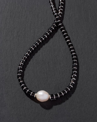 Necklace with black beads and a pearl on a dark gray background