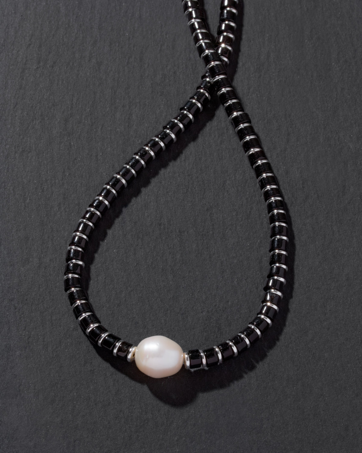 Necklace with black beads and a pearl on a dark gray background