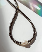 Necklace with black beads and a pearl on a white surface