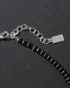 Black beaded necklace with silver chain and tag on a dark background
