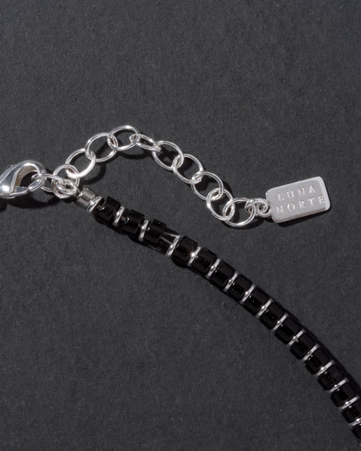 Black beaded necklace with silver chain and tag on a dark background