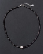 Black beaded necklace with a pearl pendant on a dark background