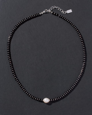Black beaded necklace with a pearl pendant on a dark background