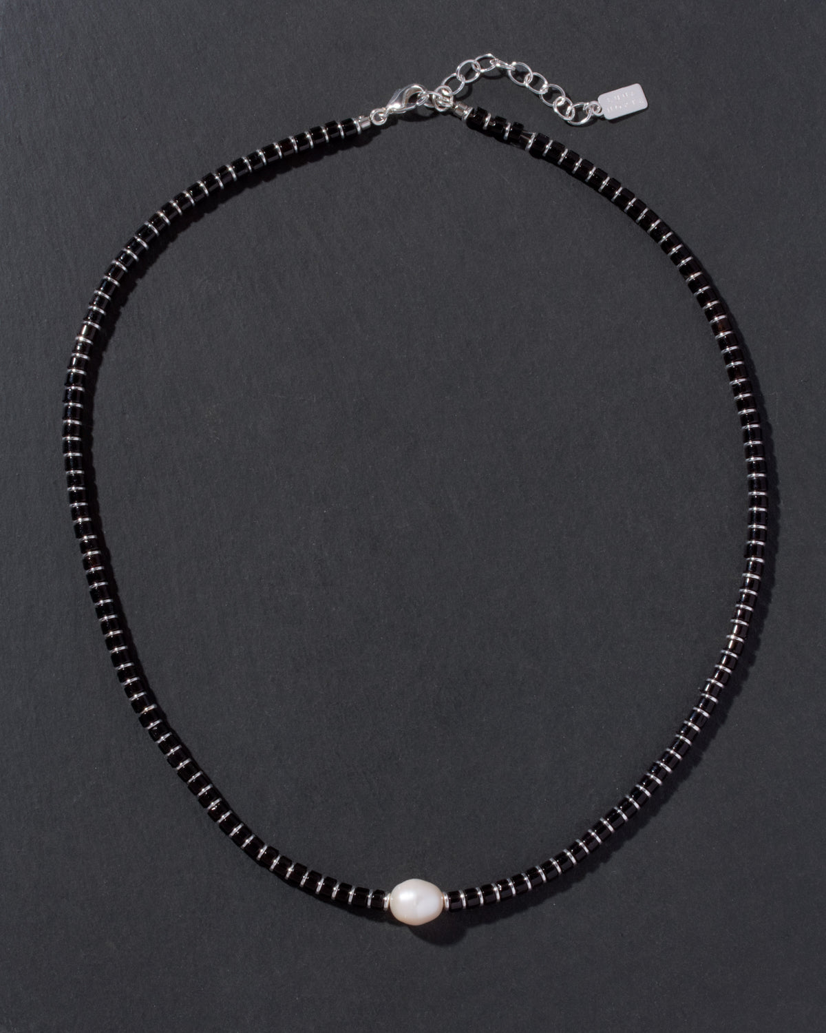 Black beaded necklace with a pearl pendant on a dark background