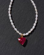 Pearl necklace with a red gemstone pendant on a dark background