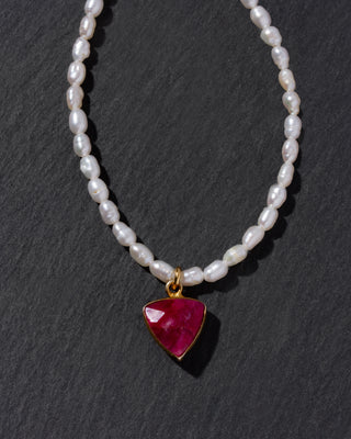 Pearl necklace with a red gemstone pendant on a dark background