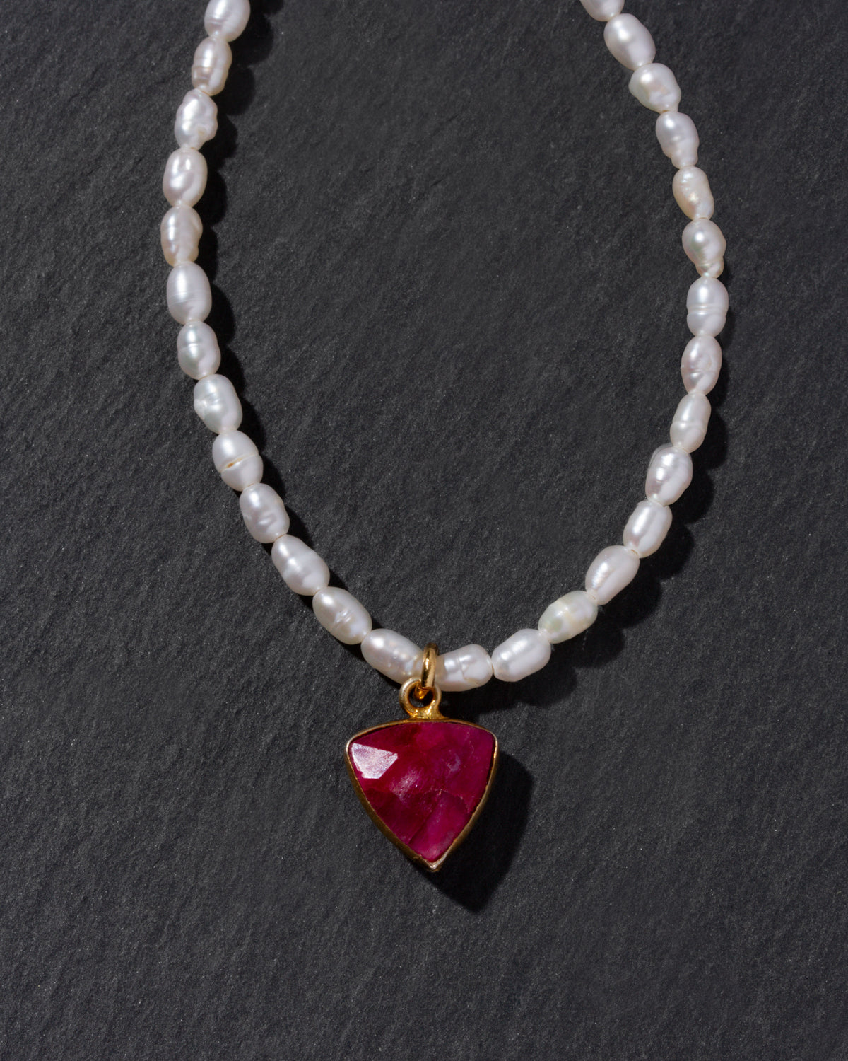 Pearl necklace with a red gemstone pendant on a dark background