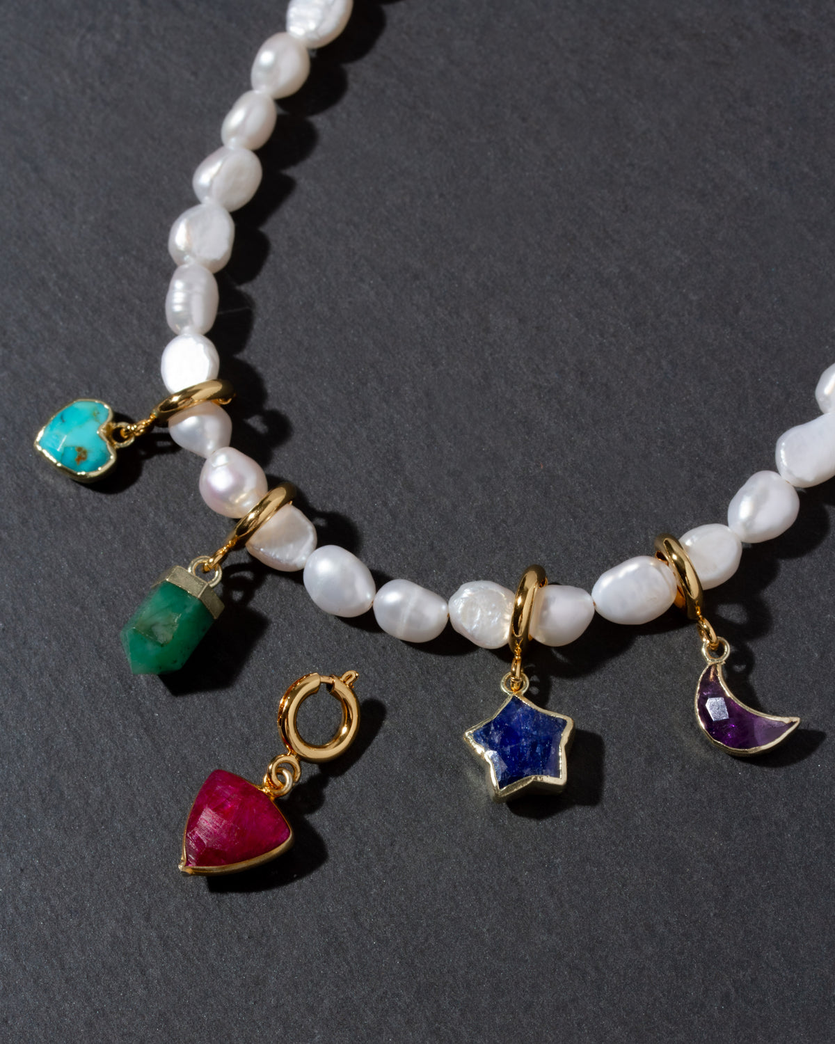 Close-up of pearl necklace with colorful gemstone charms with heart, star, moon, and pendant shapes.