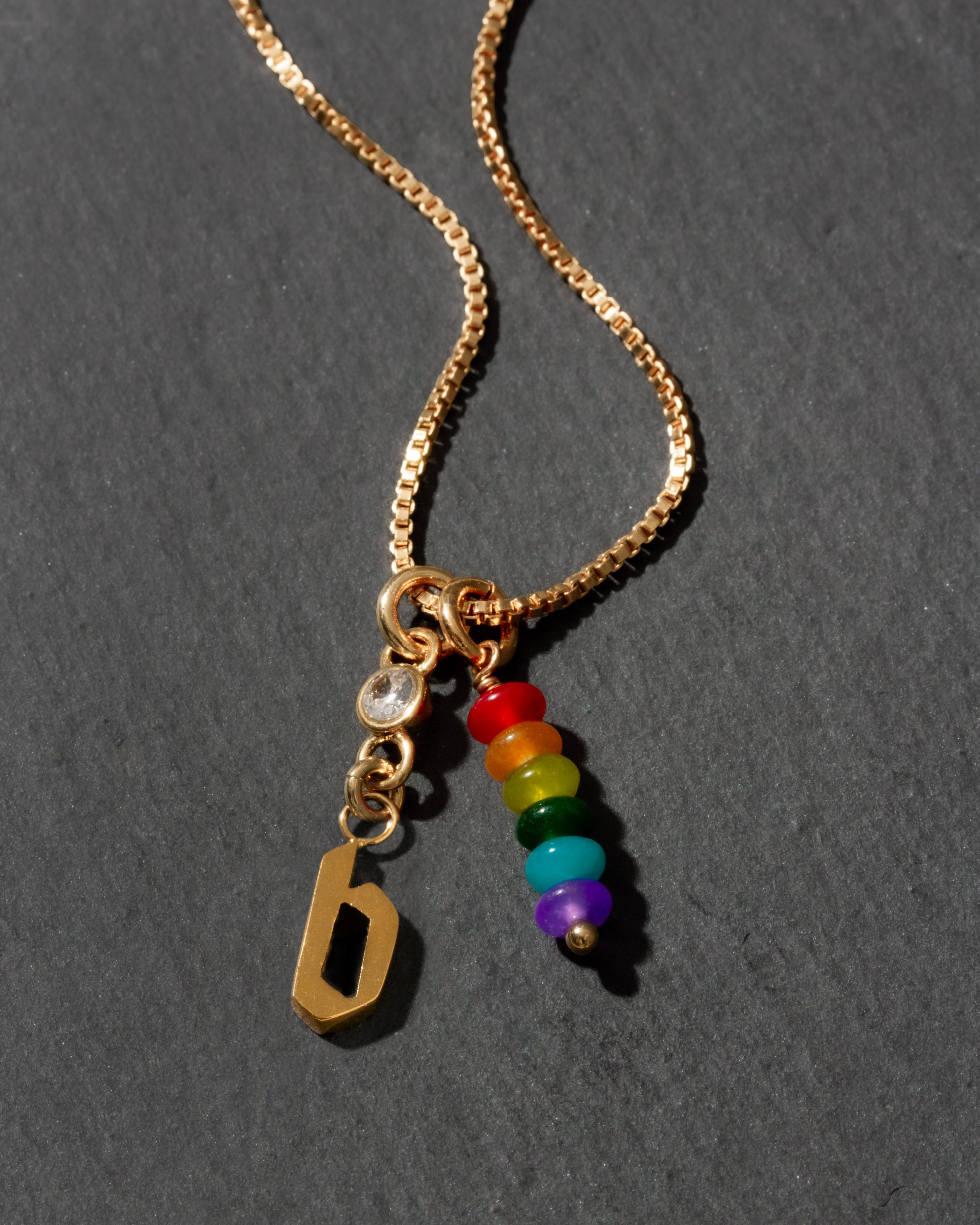 Gold necklace with rainbow beads and letter 'b' charm on a dark background