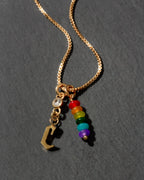 Gold necklace with rainbow beads and letter 'C' charm on a dark background