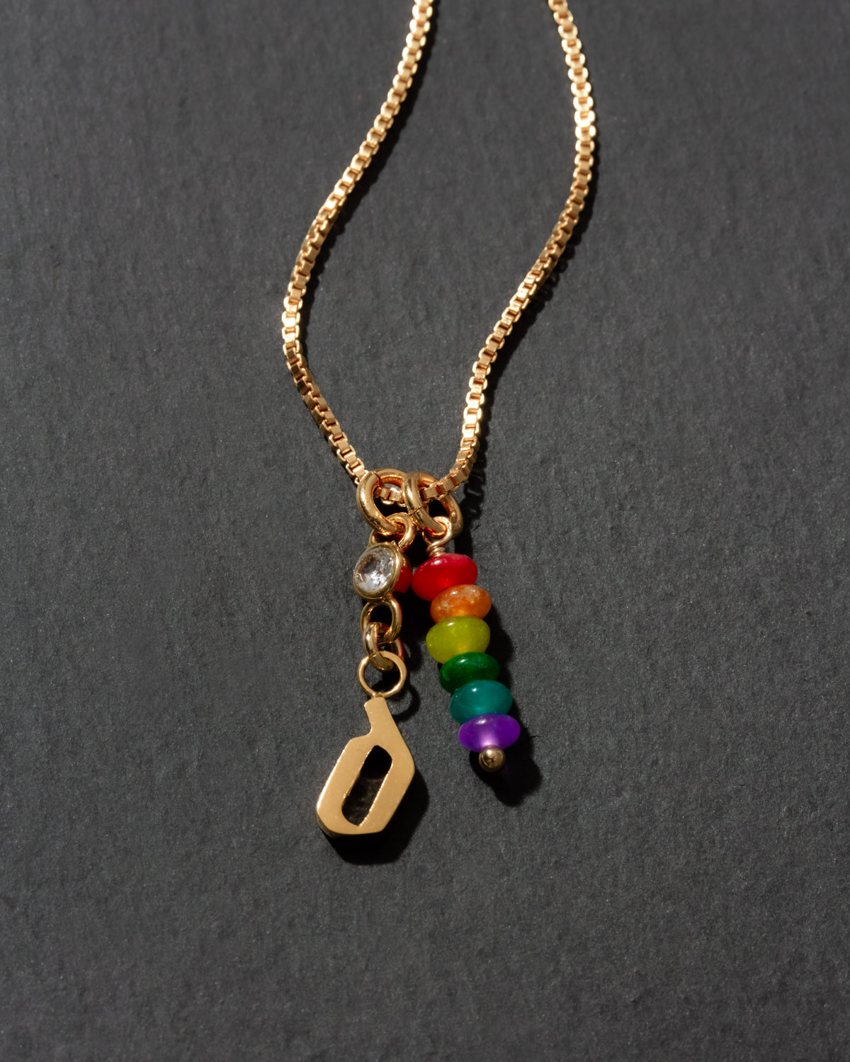 Gold necklace with rainbow charm and the letter 'd ' initial charm on a dark background