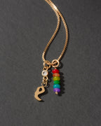 Gold necklace with rainbow charm and letter 'e' on a dark background