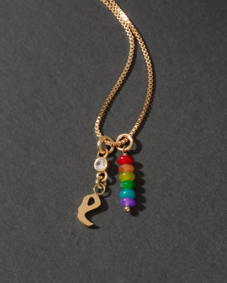Gold necklace with rainbow charm and letter 'e' on a dark background