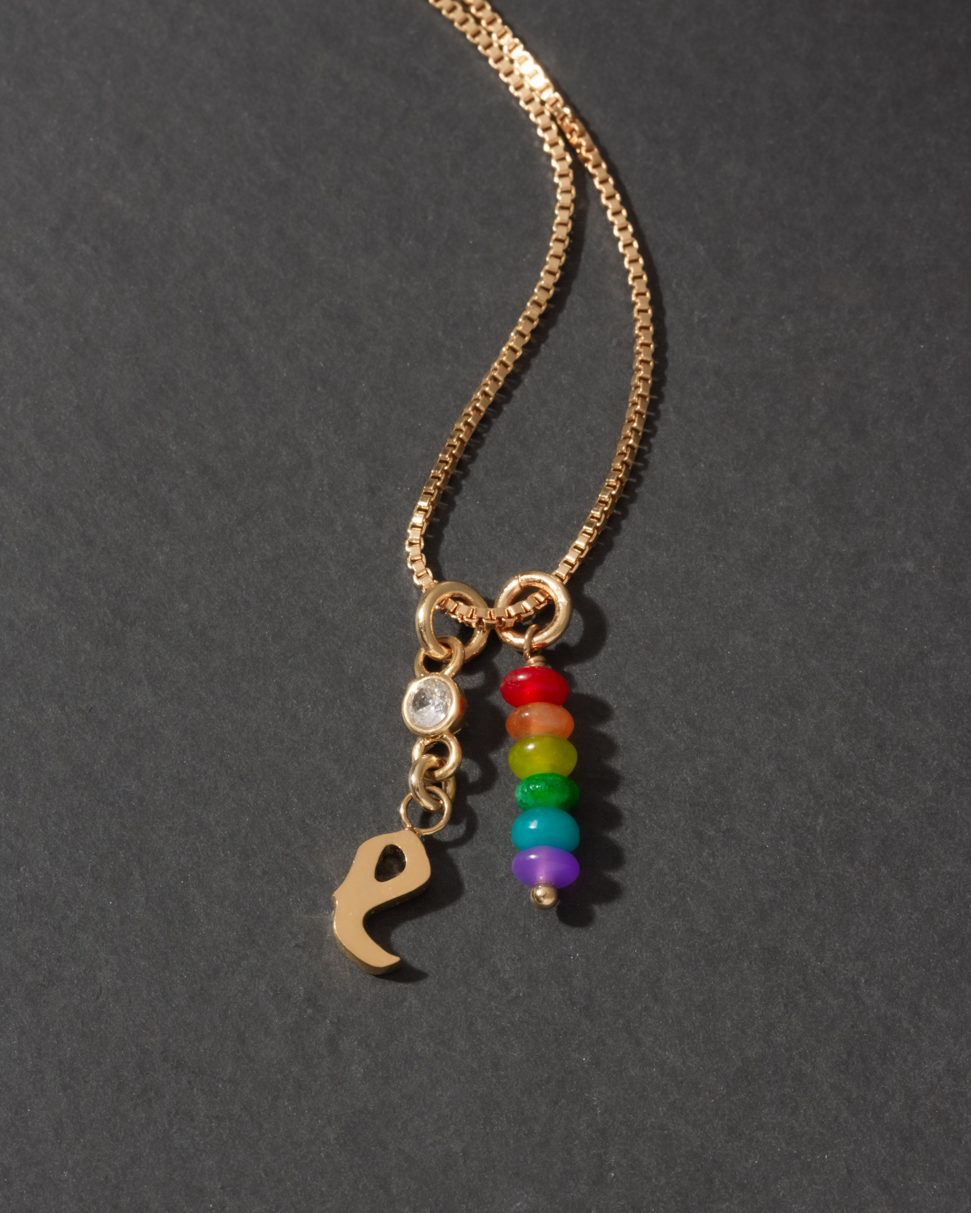 Gold necklace with rainbow charm and letter 'e' on a dark background