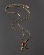Gold necklace with rainbow charm and letter 'e' initial charm on a dark gray background