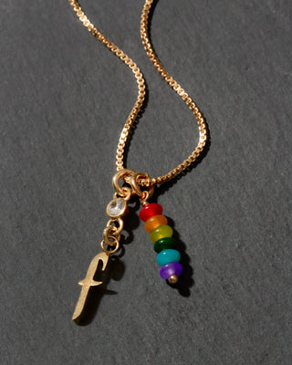 Gold necklace with rainbow beads and letter 'f' charm on a dark background