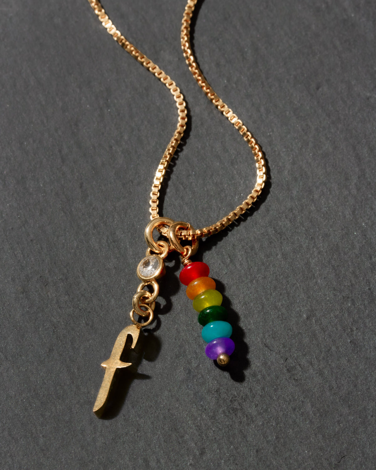 Gold necklace with rainbow beads and letter 'f' charm on a dark background