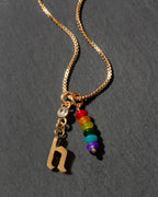 Gold necklace with rainbow beads and letter 'h' charm on a dark background