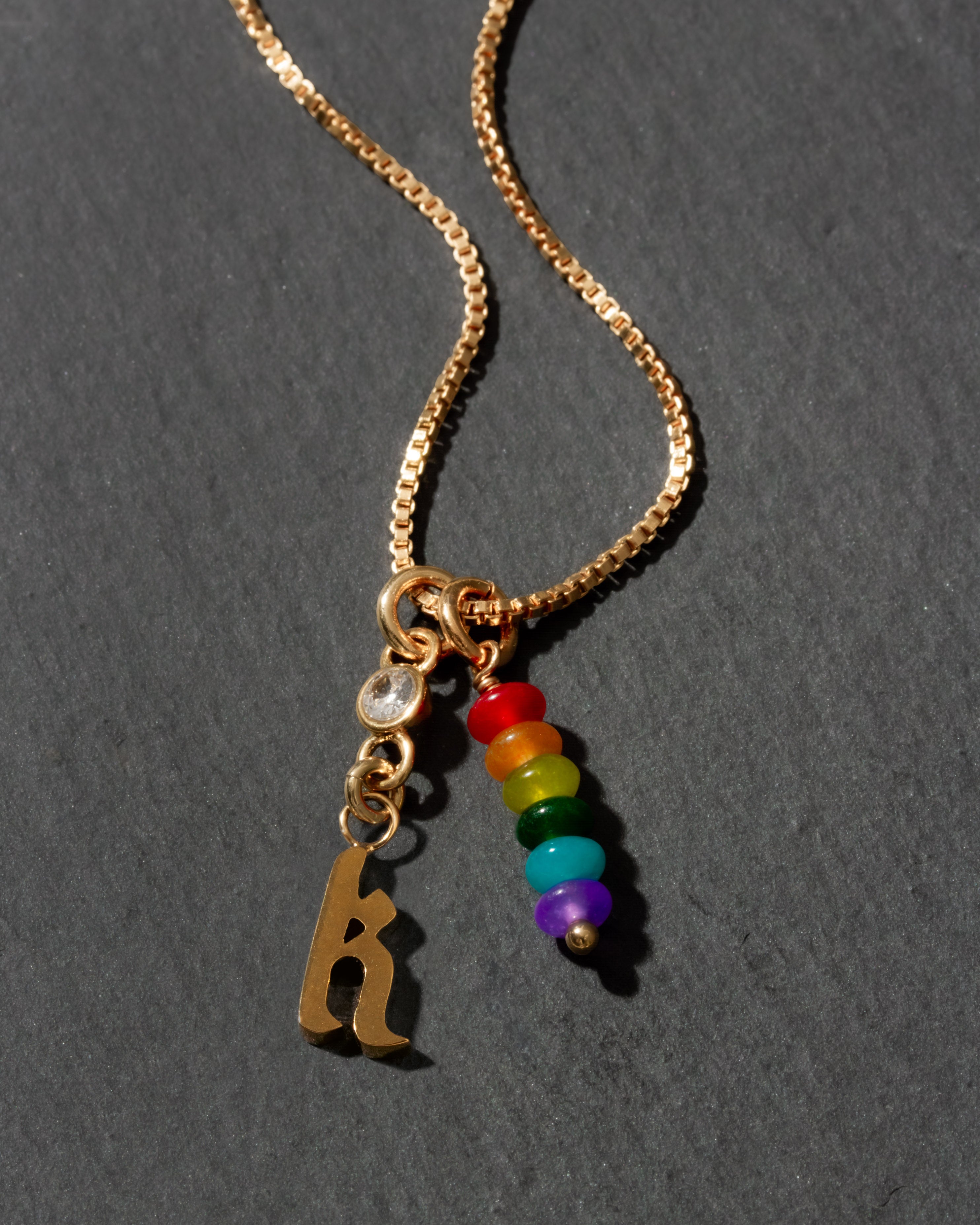 Gold necklace with rainbow beads and letter 'k' charm on a dark background