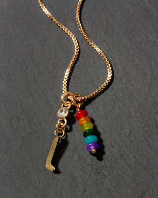 Gold necklace with rainbow charm and letter 'l' on a dark gray background