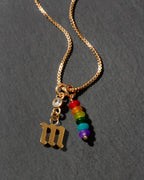 Gold necklace with a letter 'm' pendant and rainbow beads on a dark background