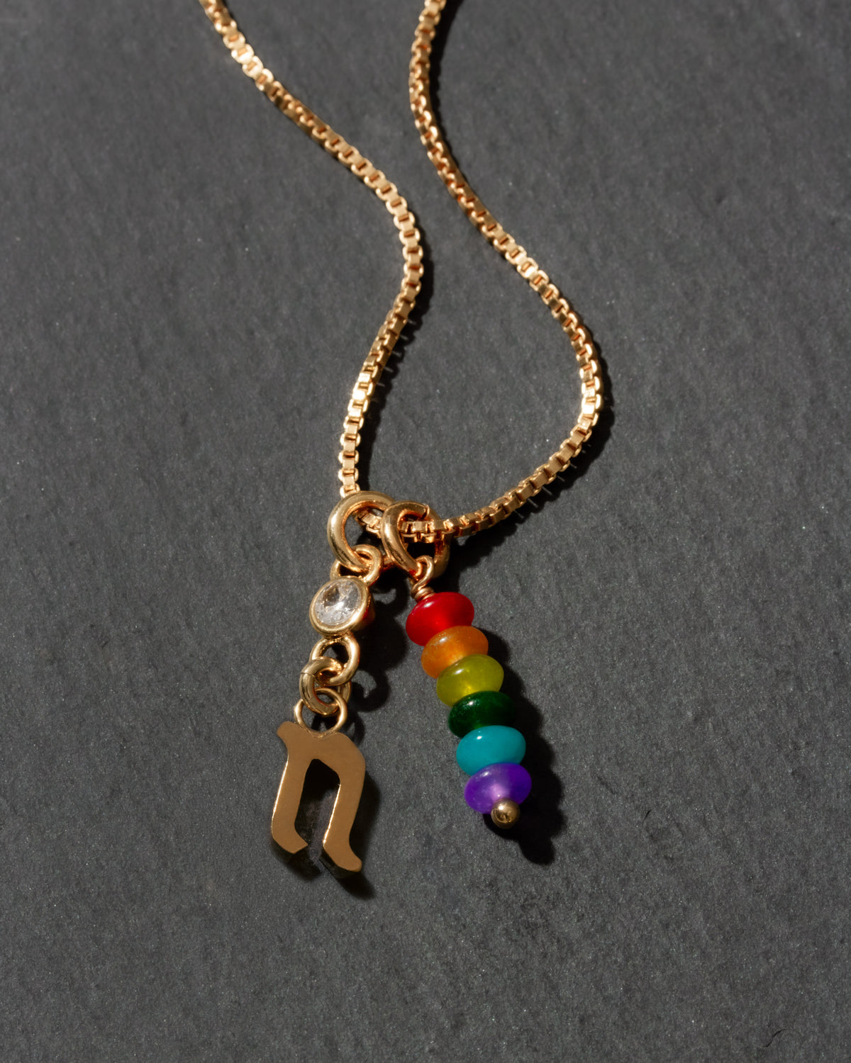 Gold necklace with rainbow beads and letter 'n' charm on a dark background