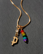 Gold necklace with rainbow charm and letter 'P' on a dark background