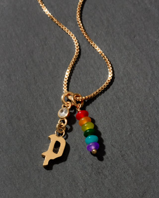 Gold necklace with rainbow charm and letter 'P' on a dark background