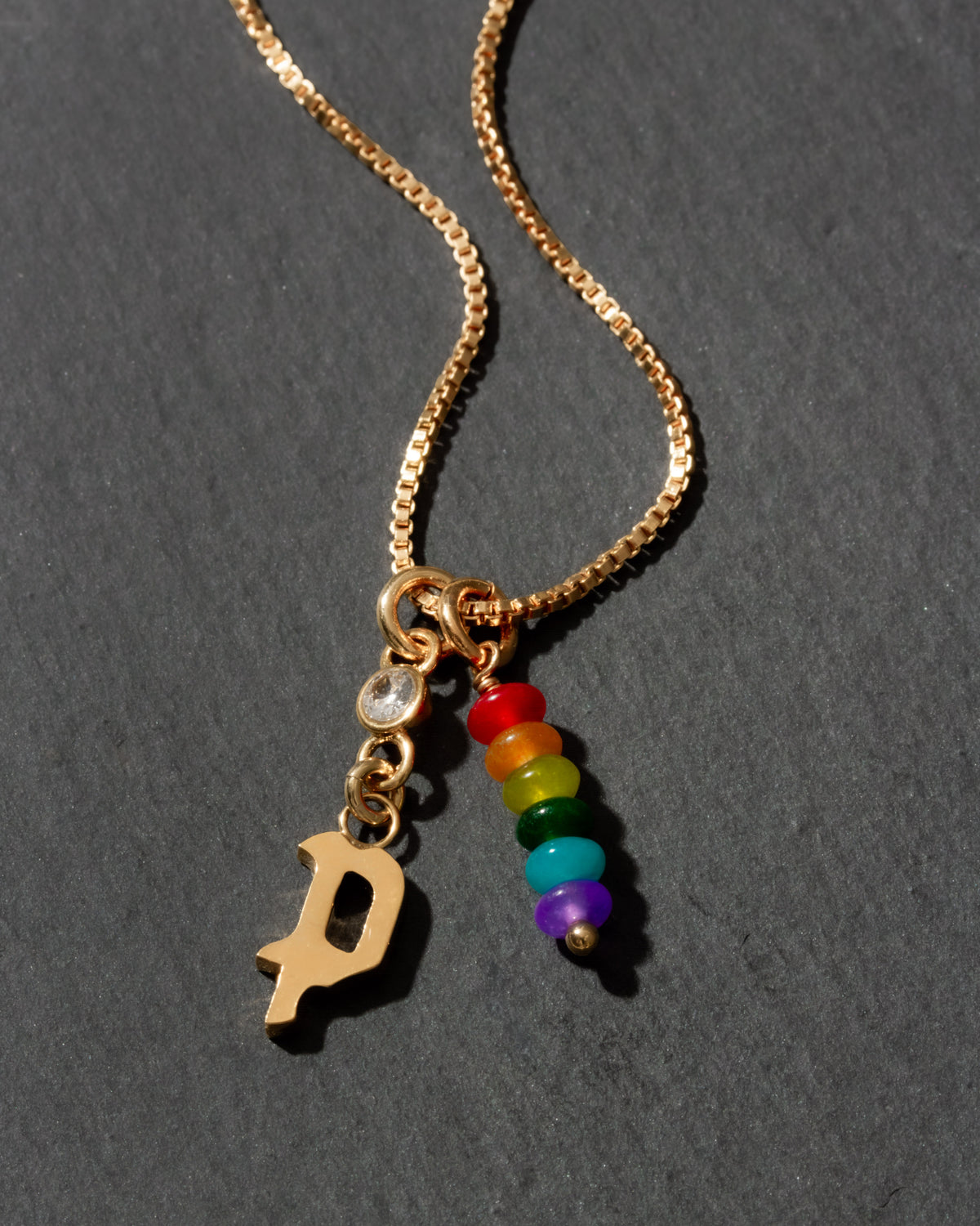 Gold necklace with rainbow charm and letter 'P' on a dark background