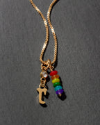 Necklace with gold chain, letter 'r' charm, and rainbow bead charms on a dark background