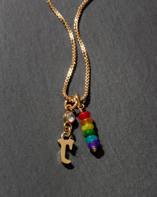 Necklace with gold chain, letter 'r' charm, and rainbow bead charms on a dark background