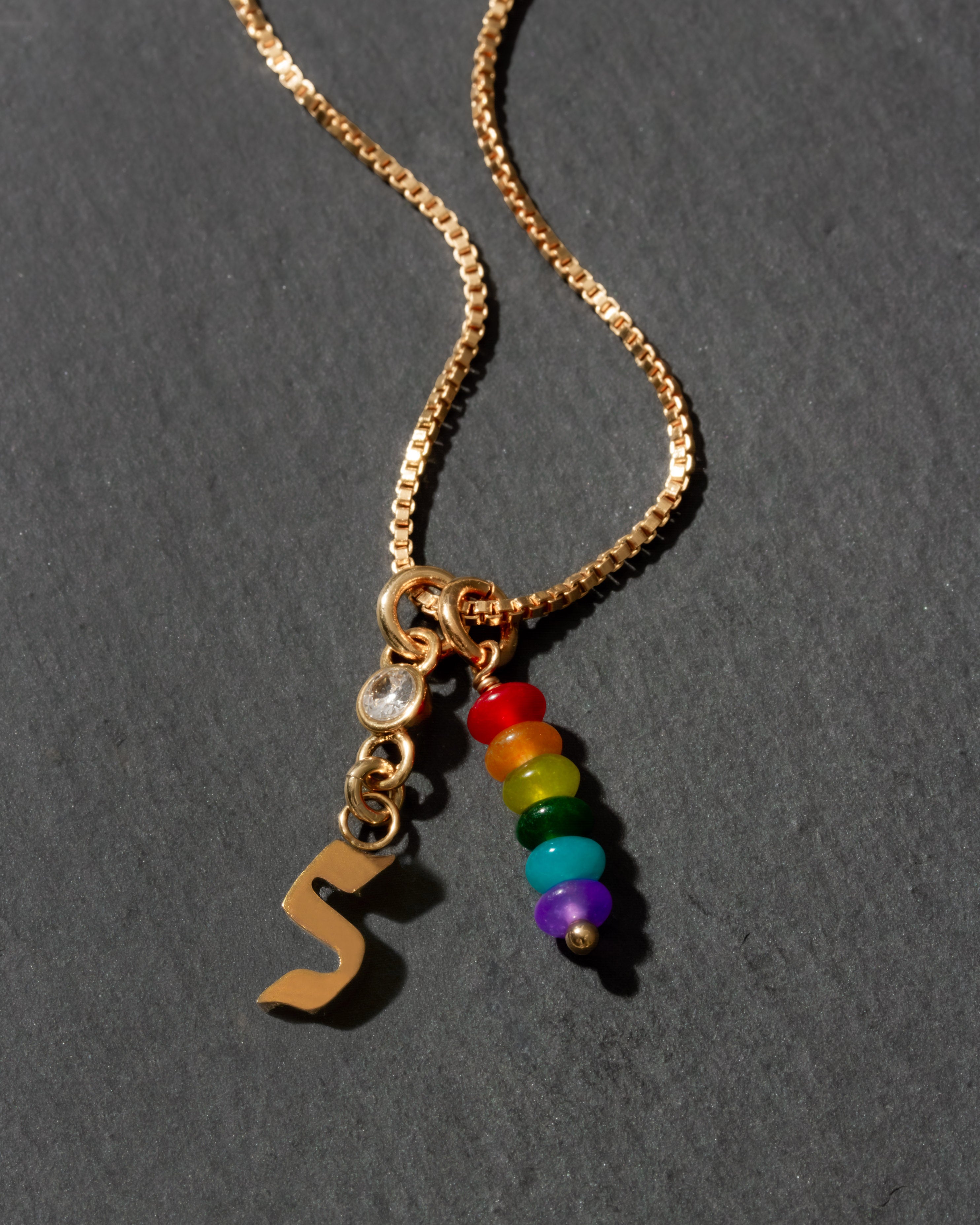 Gold necklace with rainbow beads and letter 's' charm on a dark background