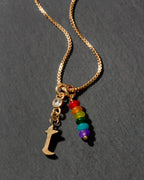 Gold necklace with rainbow beads and letter 't' charm on a dark background