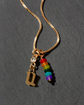 Gold necklace with rainbow beads and letter 'u' pendant on a dark background