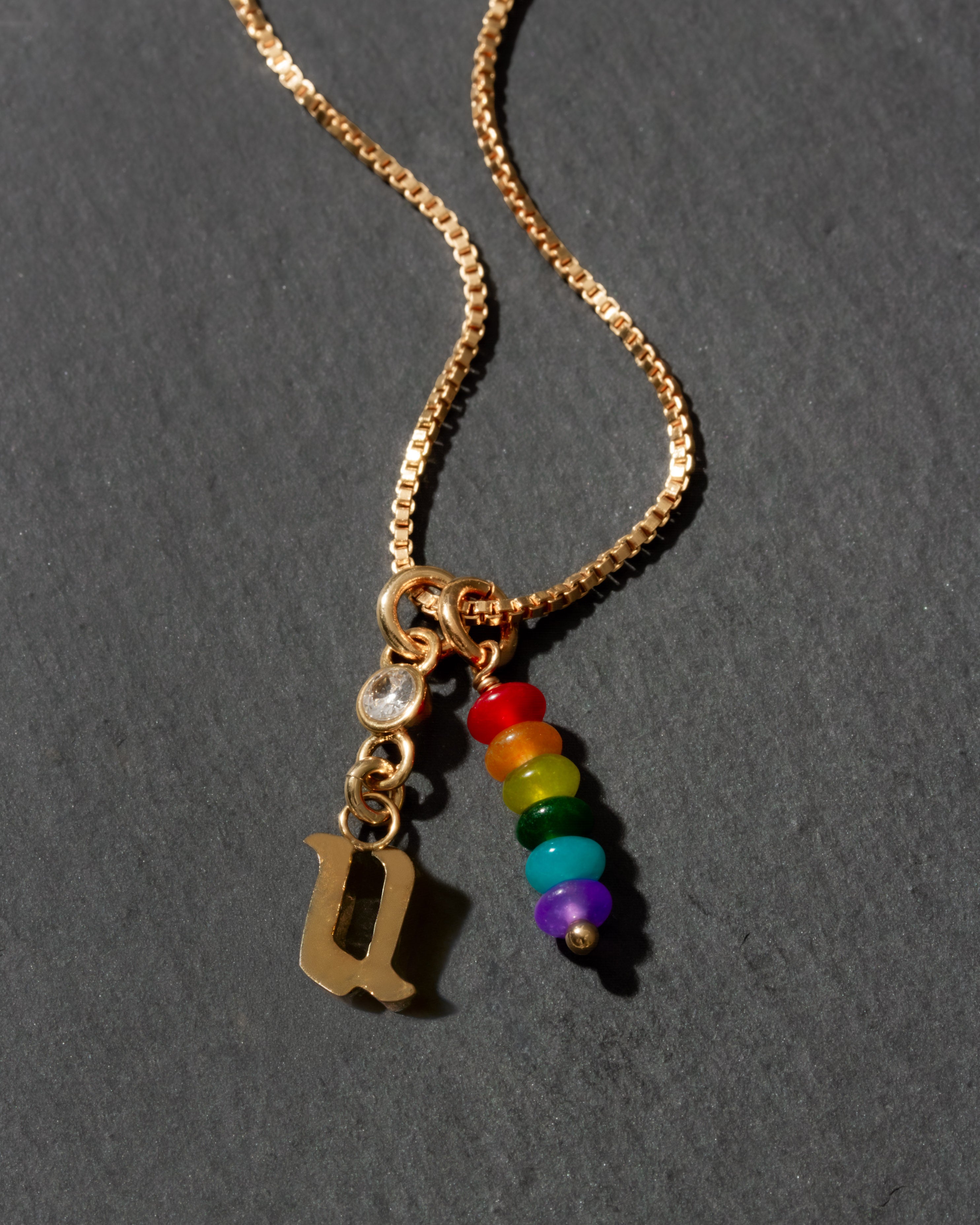Gold necklace with rainbow beads and letter 'u' pendant on a dark background