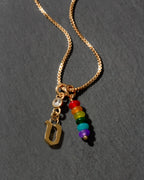 Gold necklace with rainbow beads and letter 'v' charm on a dark background