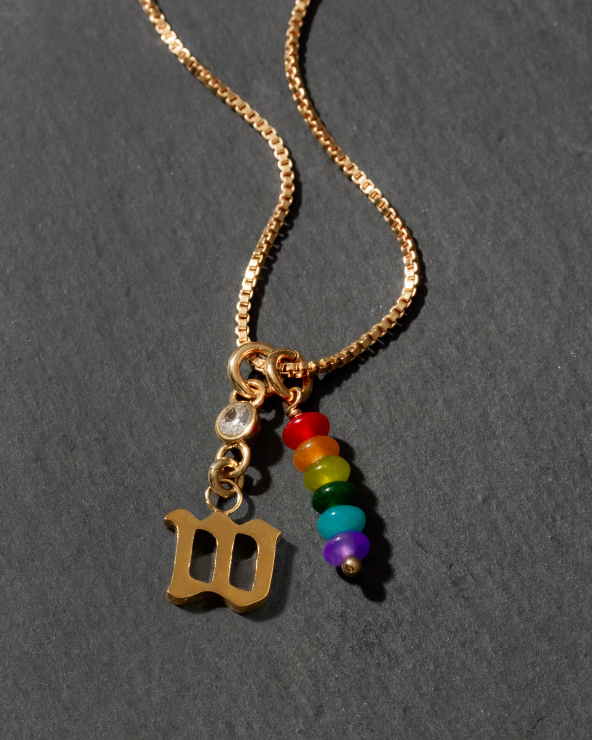 Necklace with gold pendant, rainbow beads, and letter 'W' on a dark background