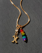 Gold necklace with rainbow charm and letter 'X' on a dark background