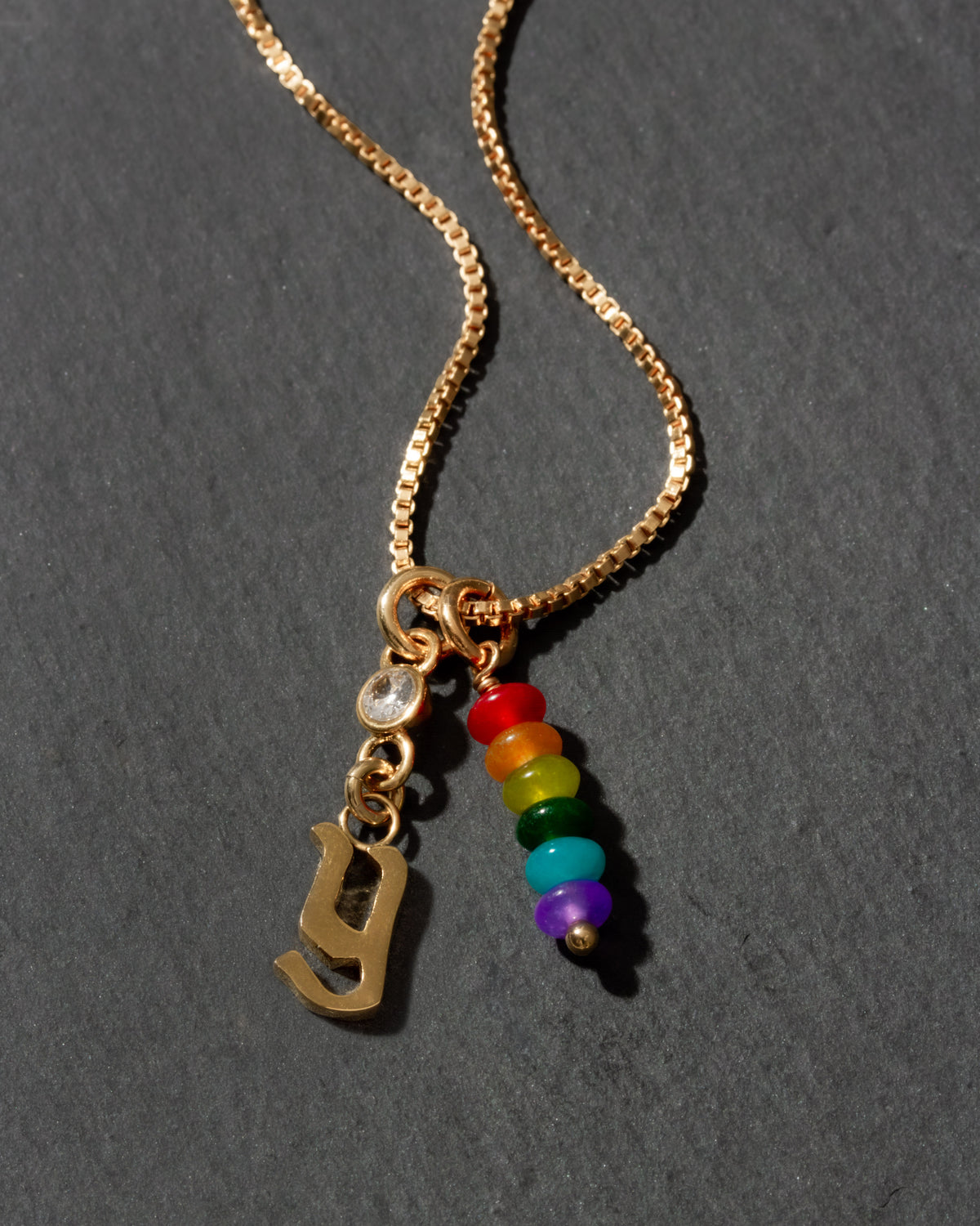 Gold necklace with rainbow beads and letter 'y' charm on a dark background