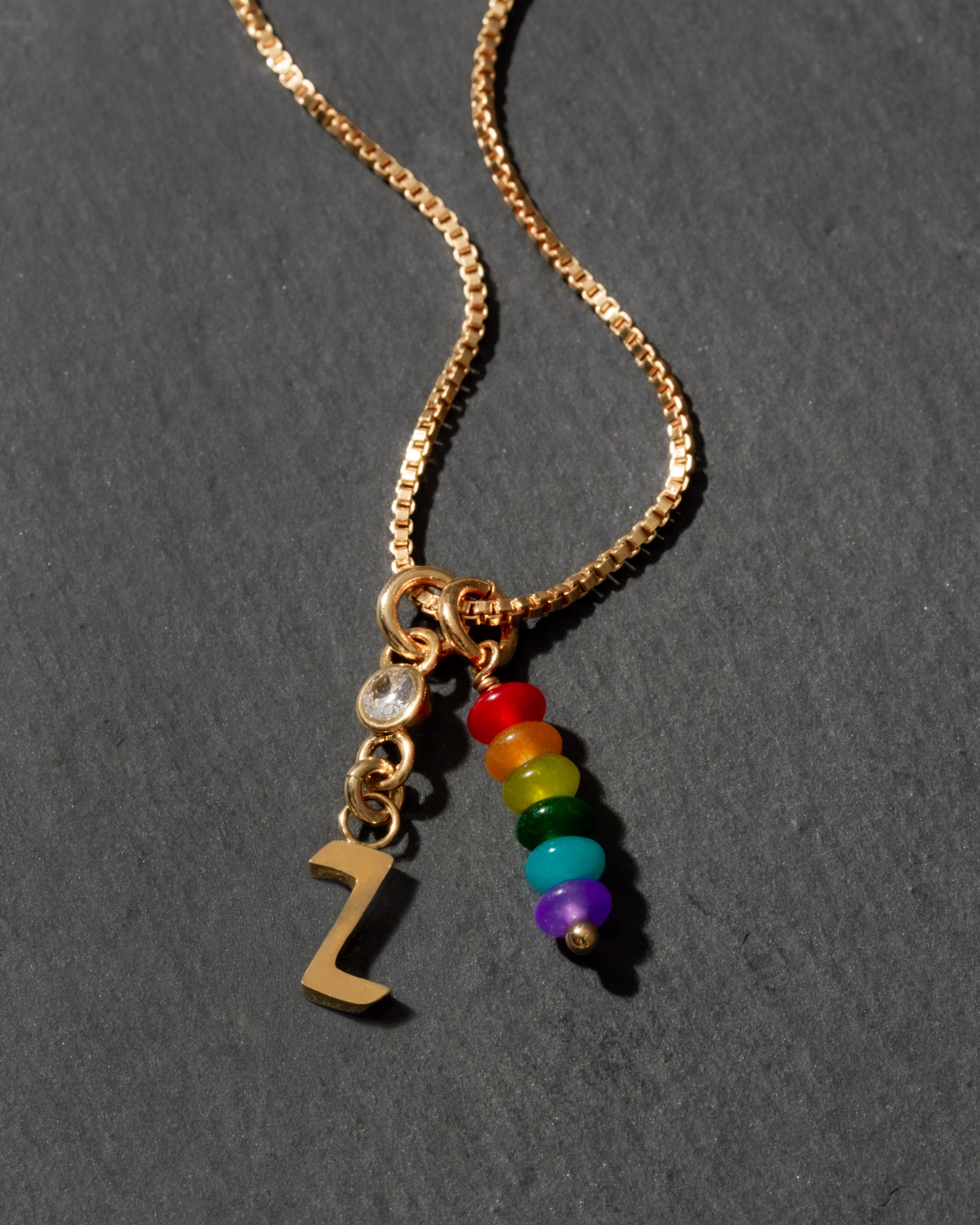 Gold necklace with rainbow charm and letter 'Z' on a dark background