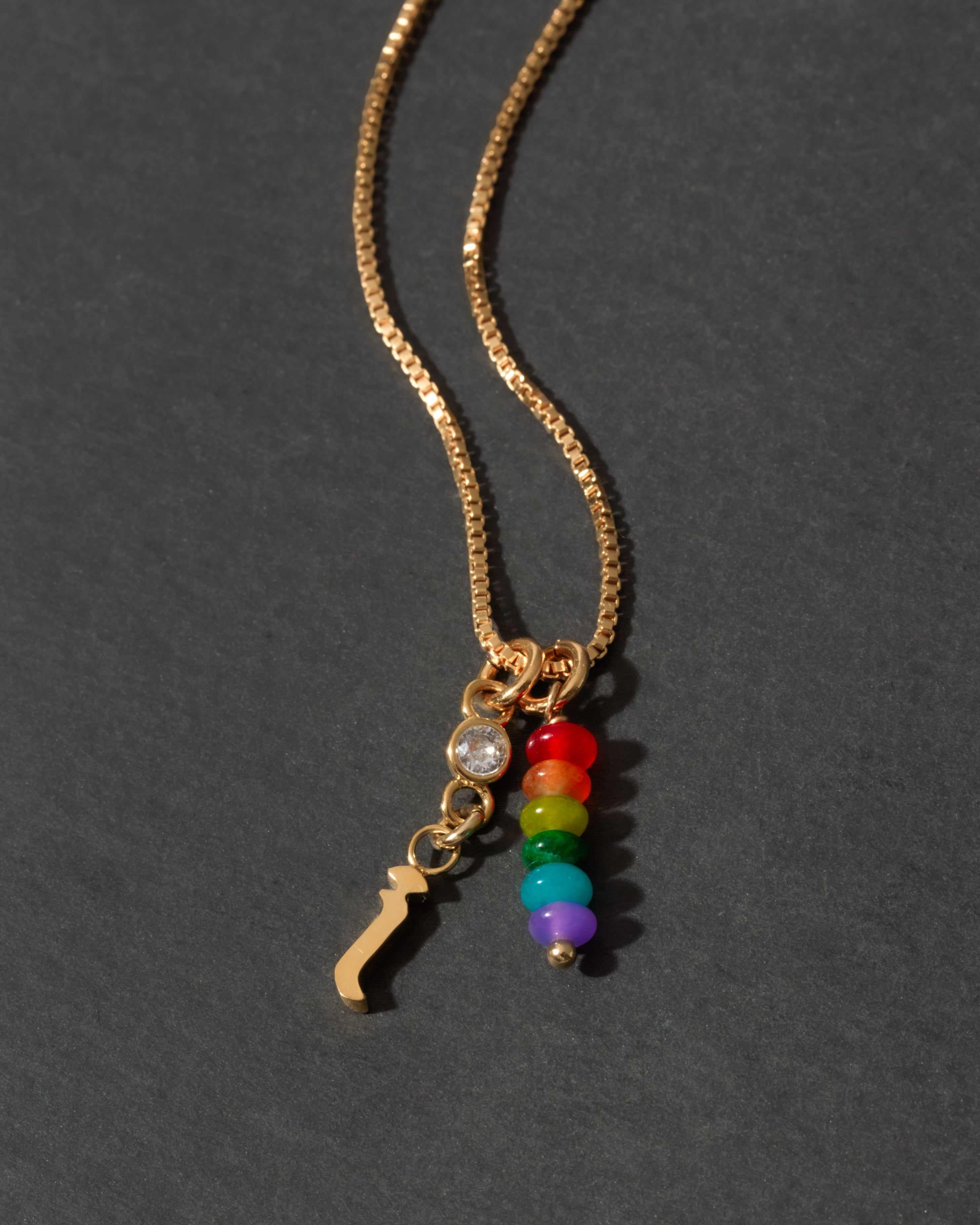 Gold necklace with colorful beads and a letter 'i' charm on a dark background