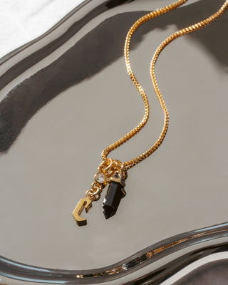 Gold necklace with letter 'c' charm and  black pendant on a reflective surface