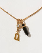 Necklace with a gold chain, a black crystal pendant, and a gold 'a' letter charm