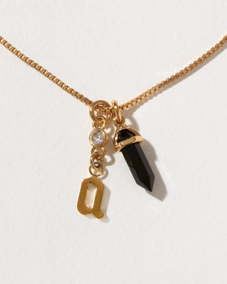 Necklace with a gold chain, a black crystal pendant, and a gold 'a' letter charm on a white background