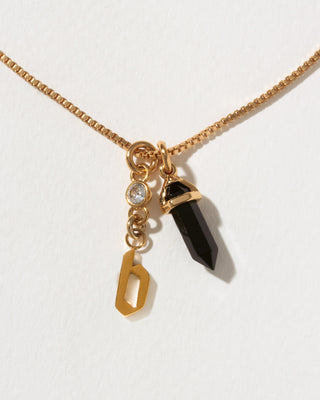 Necklace with gold chain, black crystal pendant, and gold 'b' pendant on a white background