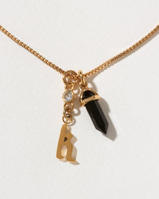 Necklace with gold chain, black crystal pendant, and letter 'k' charm on a white background