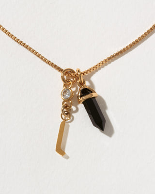 Necklace with gold chain, black crystal pendant, and gold letter 'l' charm on a white background