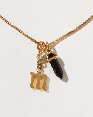Necklace with gold 'M' charm and black crystal pendant on a white background